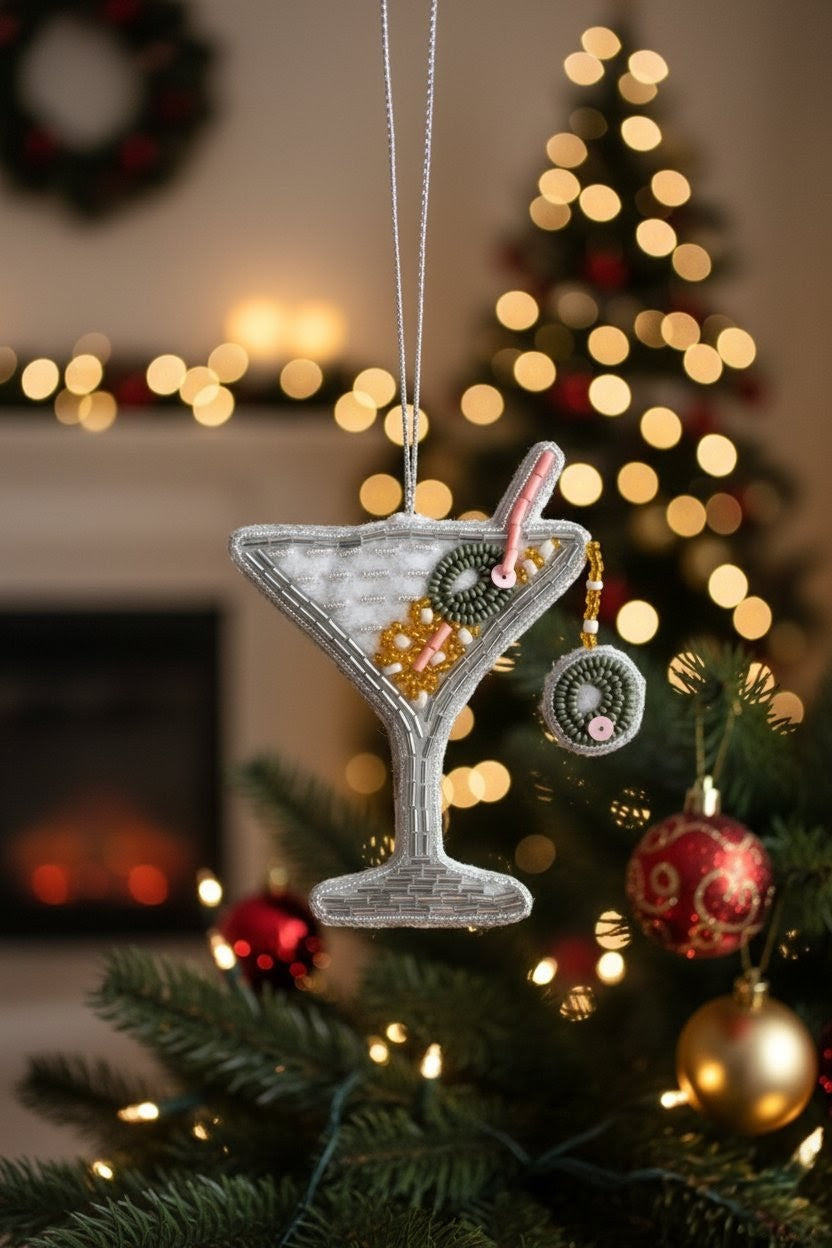 Martini Glass Ornament — A silver martini glass Christmas ornament decorated with cocktail details and a candy on a stick, hanging in front of a blurred Christmas tree and fireplace background. — Zohricanada