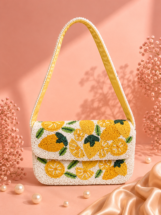 Handmade Lemon Beaded Shoulder Bag for Women | Luxury Fruit Vacation Handbag — A white beaded handbag with a yellow and green lemon pattern, featuring a yellow beaded shoulder strap, styled on a peach-pink background with decorative pearls and dried flowers. — Zohricanada
