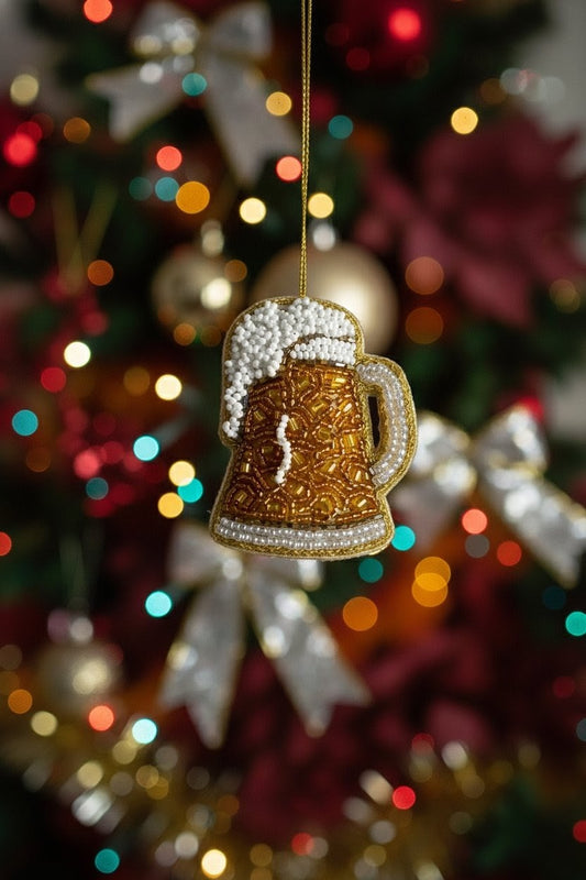 Beer Mug Ornament — A gold and white beer mug Christmas ornament hanging from a string against a blurred Christmas tree background with colorful lights. — Zohricanada