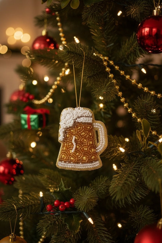 Beer Mug Ornament — A beer mug shaped Christmas ornament with a gold patterned body, white foam head, and pearl-like trim, hanging on a decorated Christmas tree with red ornaments and warm lights. — Zohricanada