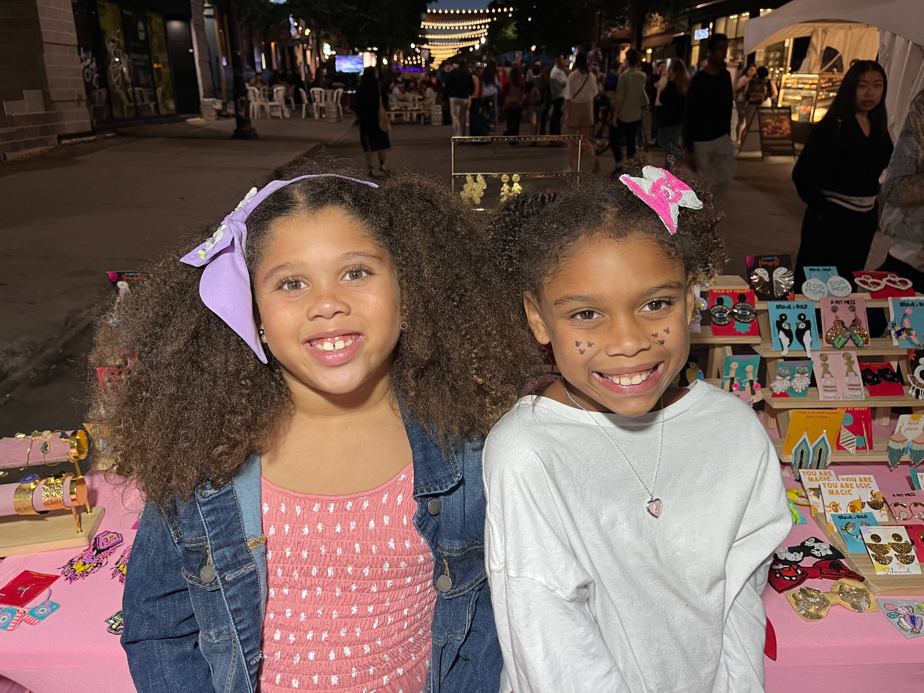 Two young customers wearing handmade beaded hair bows at a market booth | Zohricanada