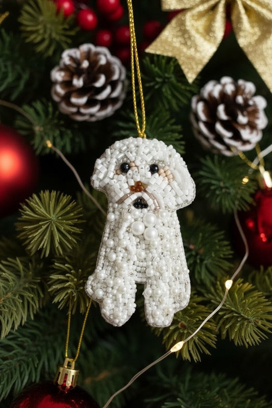 White Dog Ornament — A white beaded dog Christmas ornament hanging from a gold string on a decorated Christmas tree with pinecones, red ornaments, green needles, and fairy lights. — Zohricanada