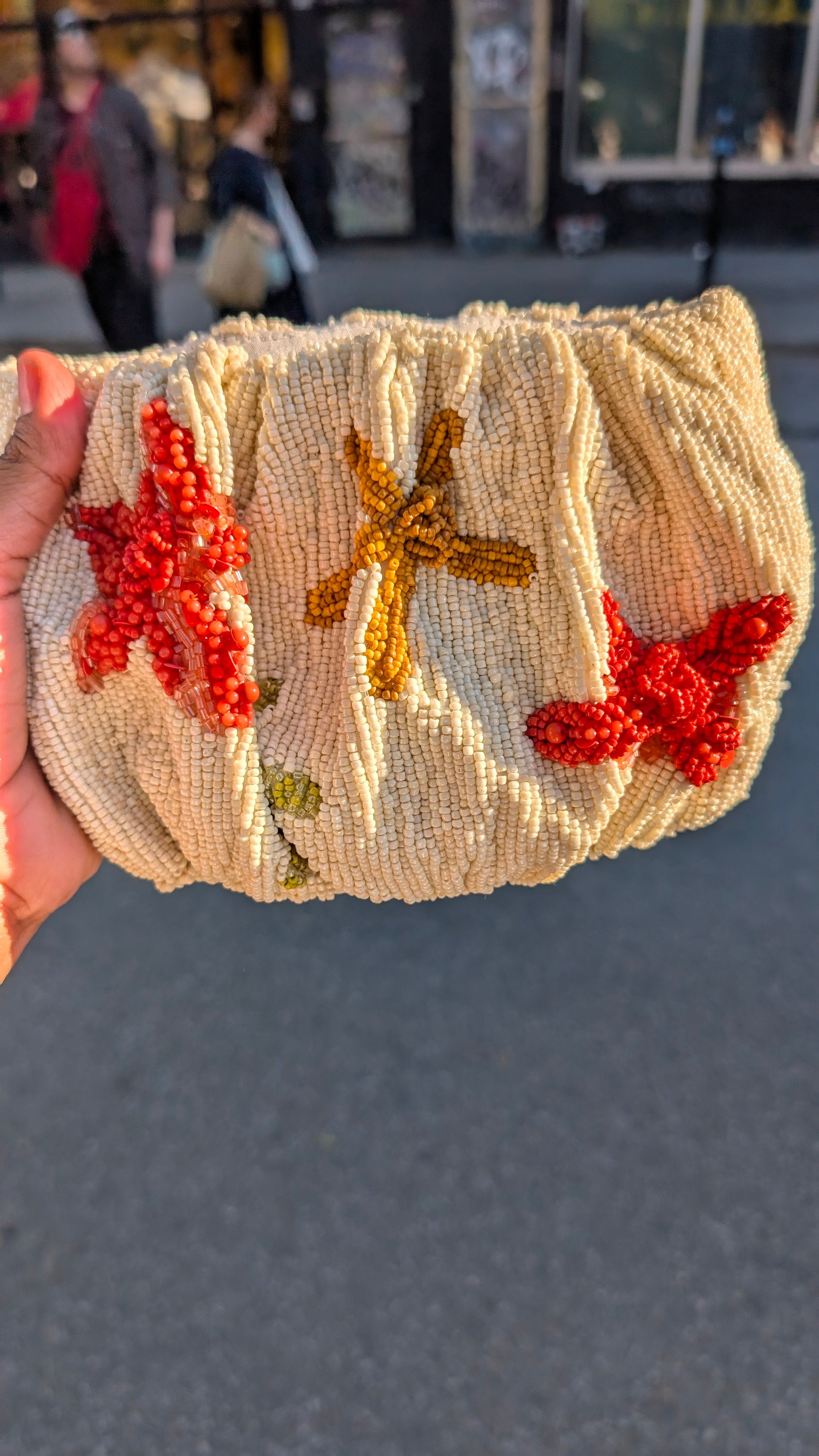Beaded clutch with starfish and butterfly designs held by a hand against an outdoor background.